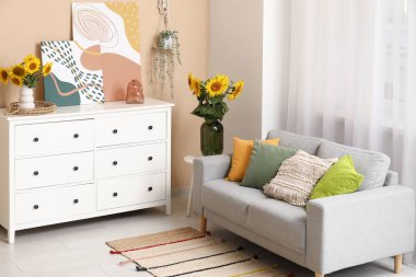 Koltuk, çekmeceler ve vazolarla dolu. Oturma odasının içinde güzel ayçiçekleri var.