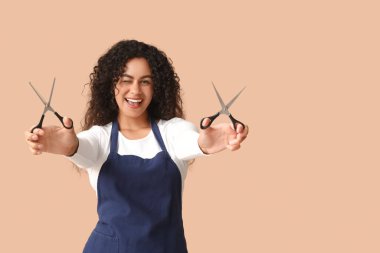 Bej arka planda makasıyla güzel, mutlu, Afro-Amerikalı bir kuaför.