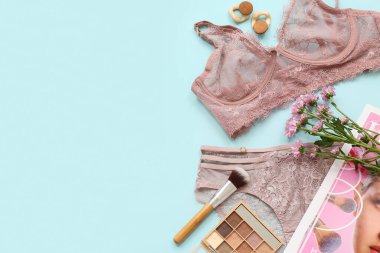 Renkli arkaplanda zarif dantel iç çamaşırları, kozmetik ürünleri ve çiçekleri olan kompozisyon