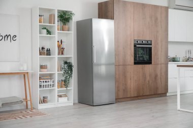 Mutfağın içinde gümüş buzdolabı ve raf ünitesi var.