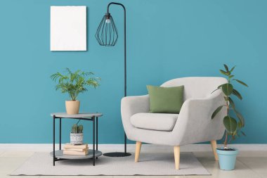 Koltuk, çiçekli kahve masası ve mavi duvarın yanında yer lambası.