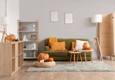 Oturma odasının sonbaharında kanepe, sehpa, puf ve çekmeceler içinde balkabağı, koni ve yapraklar.