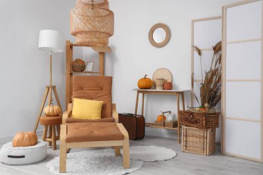 Sonbahar için tasarlanmış modern oturma odasının içinde rahat koltuk, raf ünitesi ve balkabakları var.