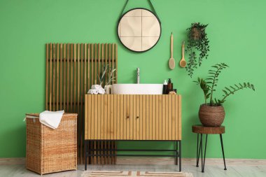 Lavabosu, çiçekleri ve yeşil duvarın yanındaki katlanabilir ekranı olan şık bir banyo.