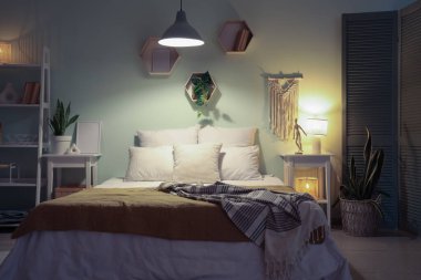 Yatak, raf ünitesi, komodinlerin, çiçeklerin ve yatak odasının iç tarafında parlayan lambaların.