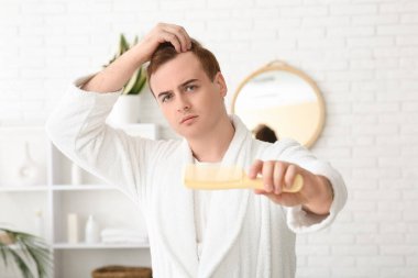 Saçları dökülen ve banyoda taranan kızıl saçlı genç adam.