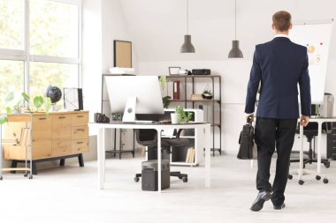 Evrak çantalı yakışıklı bir işadamı ofiste, arka planda yürüyor.