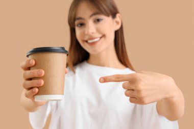 Bej arka planda bir fincan kahveye işaret eden genç bir kadın, yakın plan.