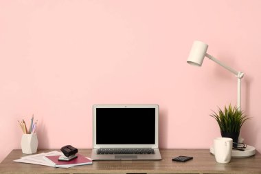 Oda pembe duvarın yanında dizüstü bilgisayarı ve kırtasiyesi olan modern işyeri