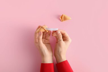 Pembe arka planda kırık fal kurabiyesi olan kadın elleri.