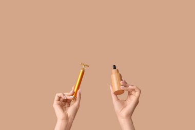 Yüz masajı silindiri ve bej arka planda gerekli yağı olan genç bir kadının elleri.