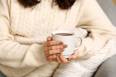 Evdeki kanepede oturan bir fincan sıcak çikolatalı güzel genç kadın.
