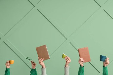 Yeşil arka planda gözlüklü, kitaplı ve fincanlı kadın eller.