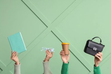 Yeşil arka planda gözlüklü, kitaplı, çantalı ve kağıt bardaklı kadın eller.