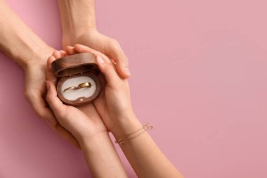 Pembe arka planda alyansları olan çift.