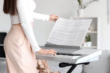 Not kâğıtlarıyla evde sentezleyici çalan genç bir kadın, yakın plan.