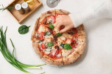 Beyaz arka planda pizza Margarita 'ya fesleğen yaprağı ekleyen kadın eli. Üst görünüm