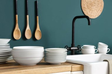 Lavabo ve ahşap masa. Mutfakta mavi duvarın yanında farklı tabaklar var.