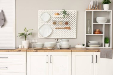 Mutfaktaki beyaz duvarın yanındaki tezgahlarda ev bitkisi, tabak, tabak ve çatal bıçak takımı var.