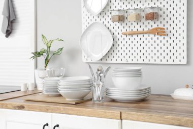 Mutfaktaki beyaz duvarın yanındaki tezgahlarda ev bitkisi, tabak, tabak ve çatal bıçak takımı var.