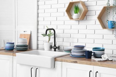Farklı tabaklar ve lavabo mutfaktaki beyaz tuğla duvarın yanında.