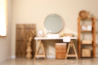 Göğüs çekmeceleri, raf ünitesi ve bej duvarın yanındaki katlama ekranlı banyo görüşü bulanık.