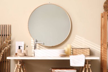 Banyodaki bej duvarın yanında lavabo, kutu ve banyo malzemeleri olan masa.