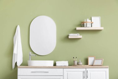 Şık banyoda yeşil duvarın yanında banyo ve lavabo aksesuarları olan çekmeceler.