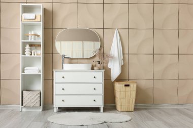 Çekmeceler, ayna ve raflar şık banyodaki bej fayanslı duvarın yanında.