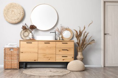 Lavabolu çekmeceler, kurumuş çiçekler ve banyo malzemeleri banyonun iç tarafındaki beyaz duvarın yanında.