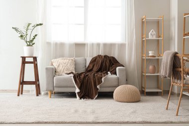 Oturma odasının iç tarafındaki pencerenin yanında kahverengi ekoseli rahat bir kanepe.