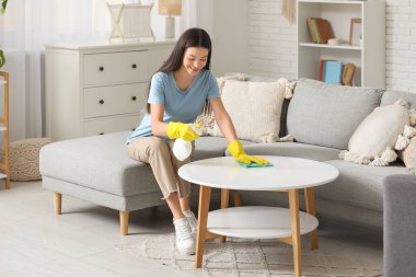 Oturma odasında bez parçasıyla masayı temizleyen genç bir kadın.