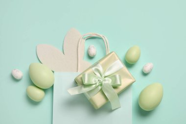 Kağıt tavşan kulaklı alışveriş torbası, Paskalya yumurtası ve turkuaz arka planda hediye kutusu.