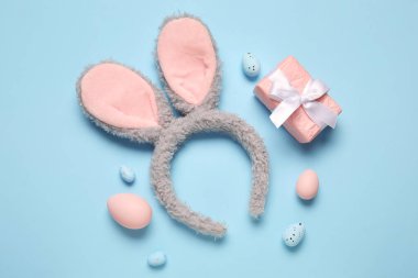 Mavi arka planda Paskalya yumurtası ve hediye kutusu olan tavşan kulakları.