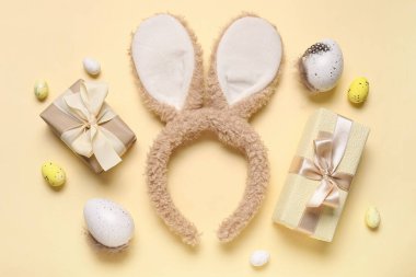 Paskalya yumurtalı tavşan kulakları ve bej arka planda hediye kutuları.