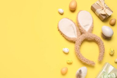 Paskalya yumurtalı tavşan kulakları ve sarı arka planda hediye kutuları.