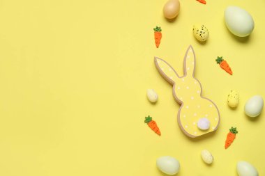 Süslü havuçlu ahşap tavşan ve sarı arka planda Paskalya yumurtası.