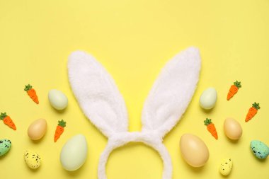 Paskalya yumurtalı tavşan kulakları ve sarı arka planda dekoratif havuçlar.