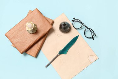 Kitaplı eski kağıt çarşaf, tükenmez kalem, mürekkep hokkası ve mavi arka planda gözlük.