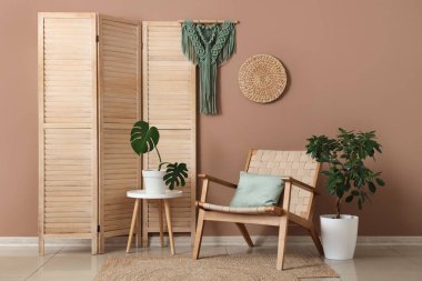 Katlanan ekran, hasır koltuk ve kahverengi duvarın yanındaki bitkiler.