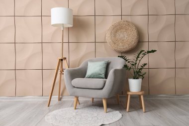 Oda içinde yer lambası, rahat koltuk ve bej döşeme duvarı yanında bitki örtüsü var.