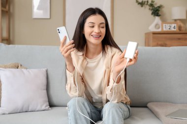 Modern elektrik bankası ve cep telefonu olan güzel bir kadın evdeki koltukta oturuyor.