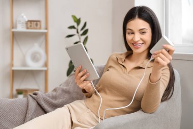 Evde tablet bilgisayar kullanan, modern güç bankası olan güzel genç bir kadın.