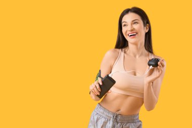 Modern güç bankasına sahip genç bir kadın sarı arka planda kablosuz kulaklıkları şarj ediyor.