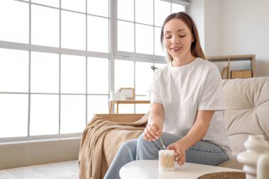 Evde kanepede oturan pamuklu tomurcuklu genç bir kadın.