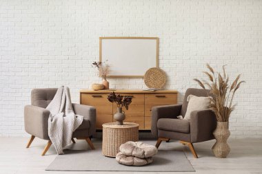 Koltuklar, kahve masası ve beyaz tuğla duvarın yanındaki çekmeceler.