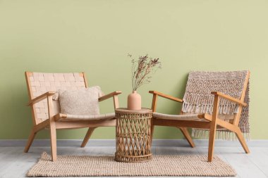 Hasır koltuklar ve vazodaki çiçekler yeşil duvarın yanındaki sehpanın üzerinde.