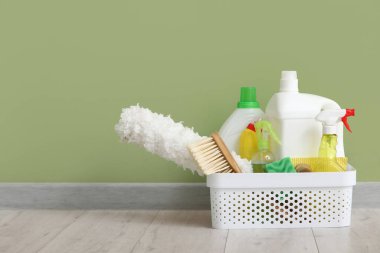 Yeşil duvara karşı lamine zemin üzerinde temizlik ürünleri dolu sepet