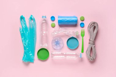 Farklı kapaklı plastik şişeler, çöp torbaları, pembe arka planda çatal ve ip.