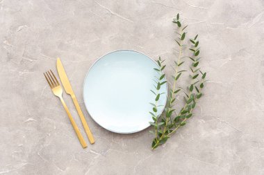 Gri grunge arka planında tabak, çatal bıçak ve bitki dallarıyla şık masa ayarları